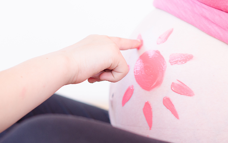 Bauch einer Schwangeren Frau mit Fingerfarben bemalt