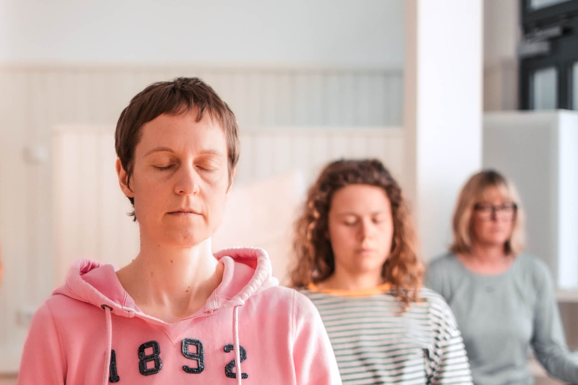 Drei gestaffelt hintereinander sitzende Frauen in Meditation