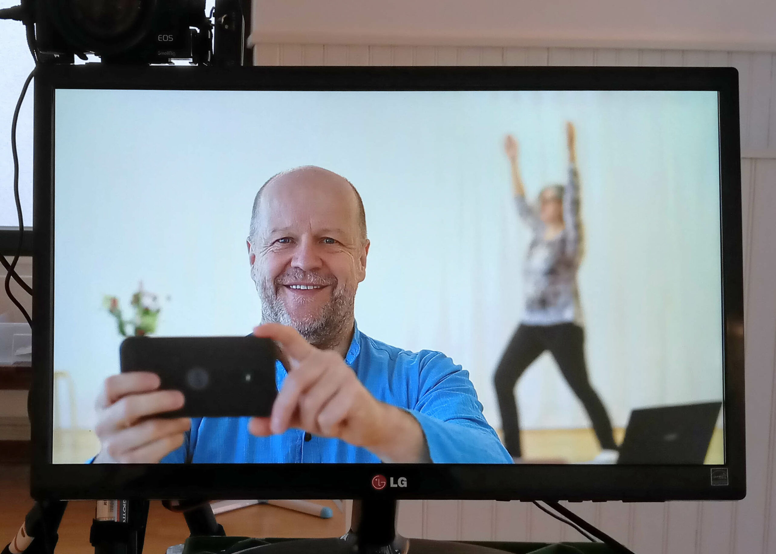 Bild im Bild mit Mann mit Handy und yogaübender Frau im Hintergrund