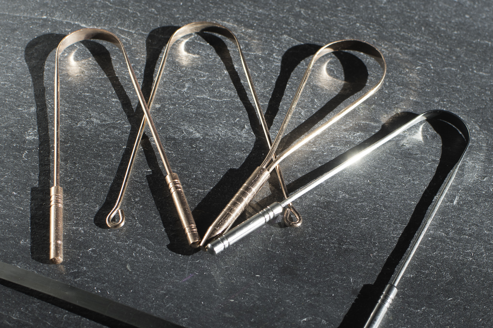 Ayurvedische Zungenschaber aus Kupfer und Edelstahl in verschiedenen Ausformungen auf Grannitplatte