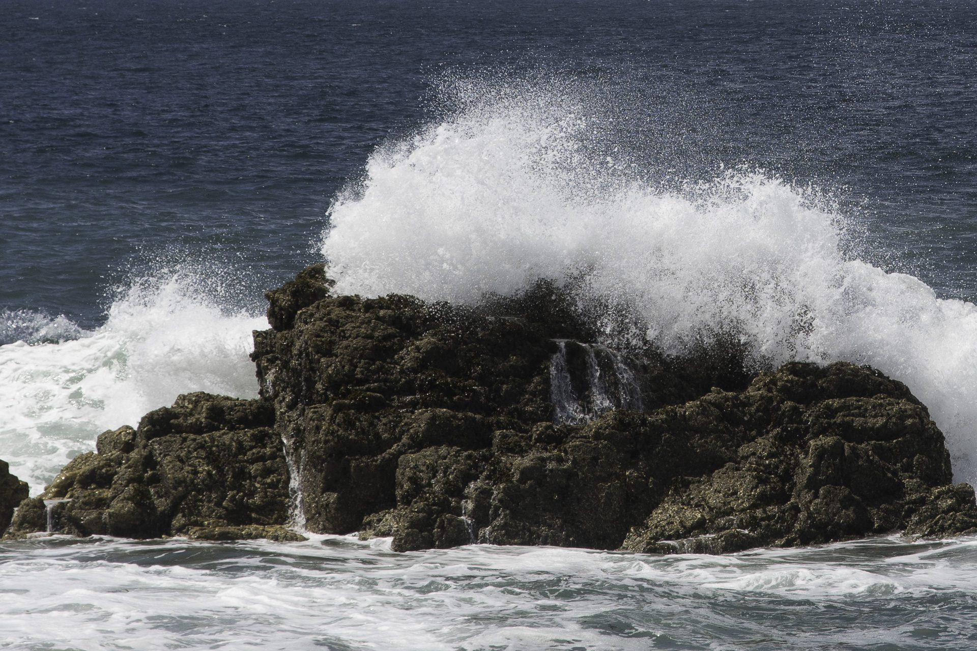 Tosendes Meer und Felsformation im Vordergrund und ruhigeres Meer im Hintergrund als Symbol für kapha-dosa in der Ayurvedalehre